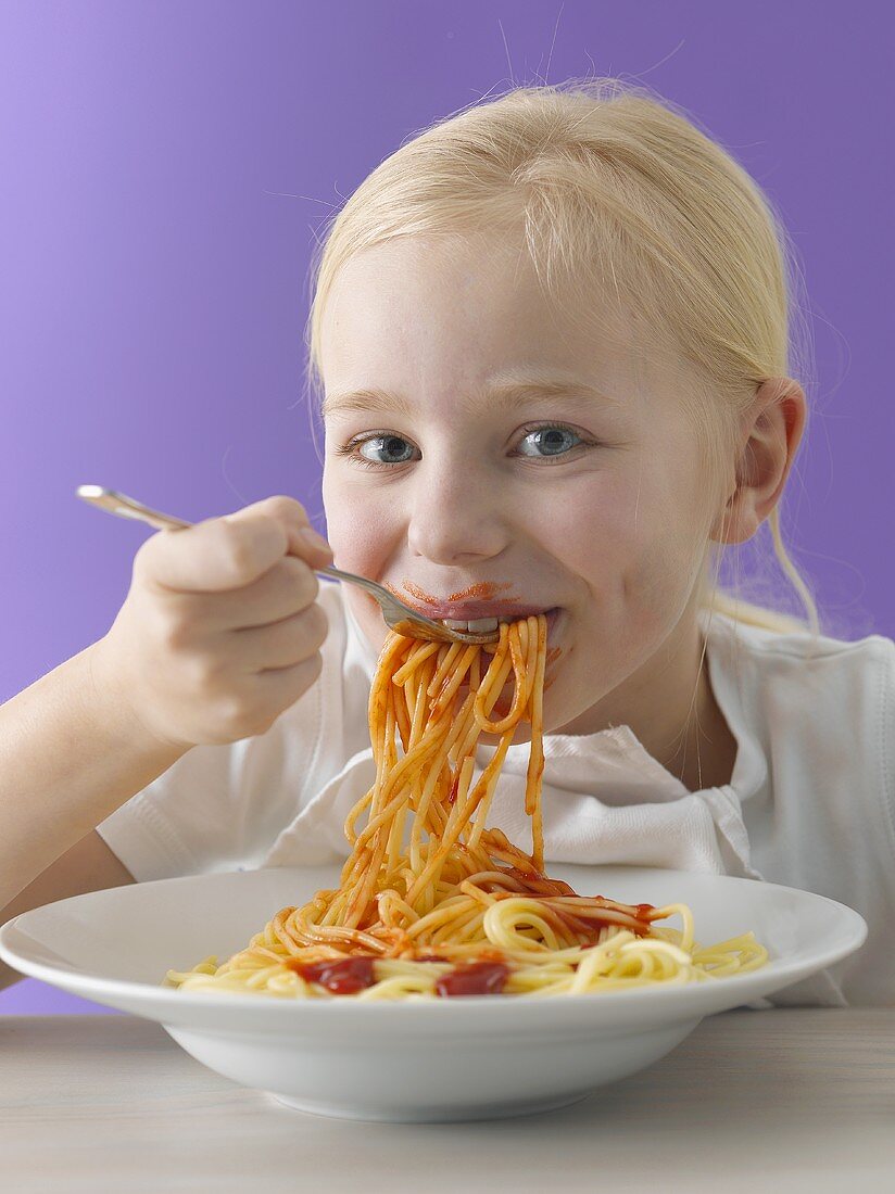 A blonde girl eating spaghetti with tomato sauce