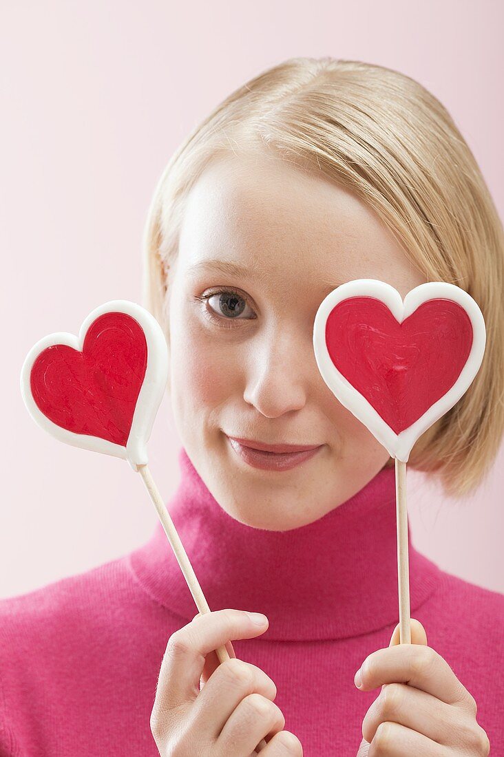 Young woman with heart-shaped lollipops in front of her eyes
