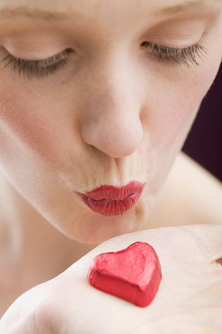 Young woman kissing red chocolate heart