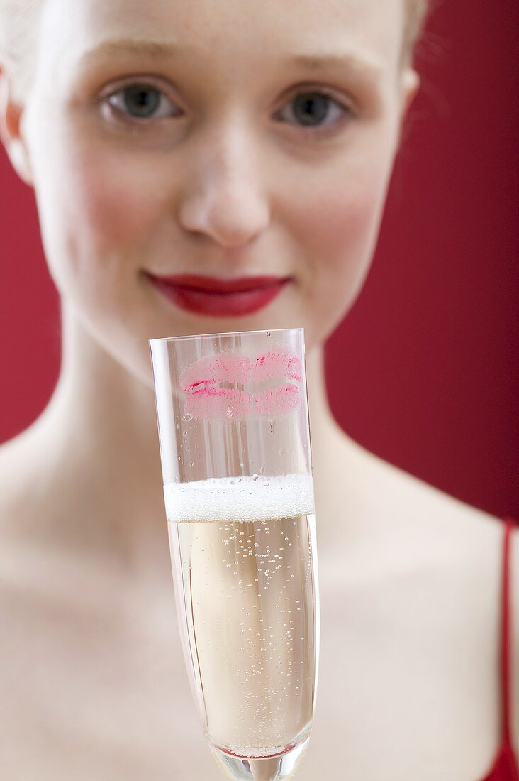 Young woman holding glass of sparkling wine with lipstick mark