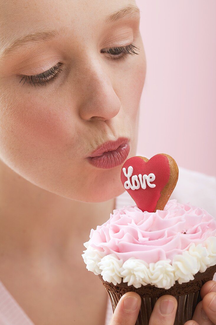 Junge Frau küsst einen Cupcake (Valentinstag)