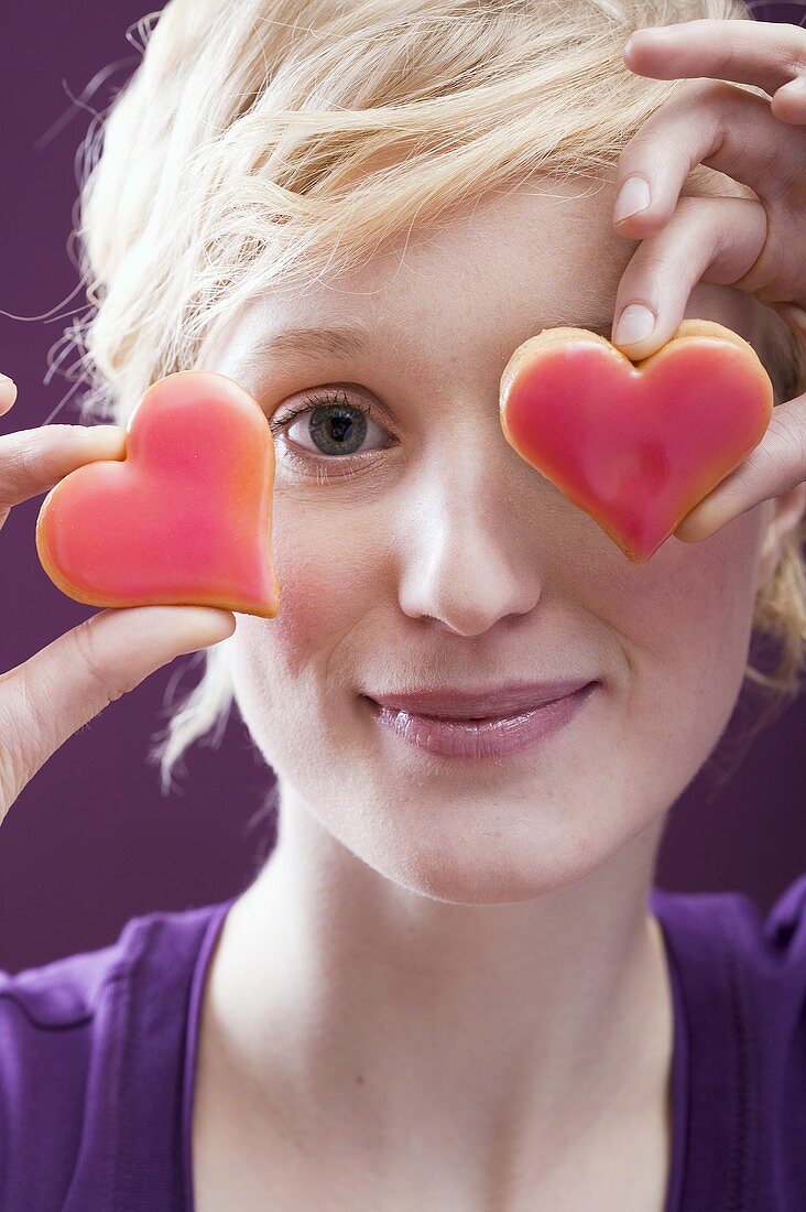 Young woman with two heart-shaped biscuits in front of her eyes