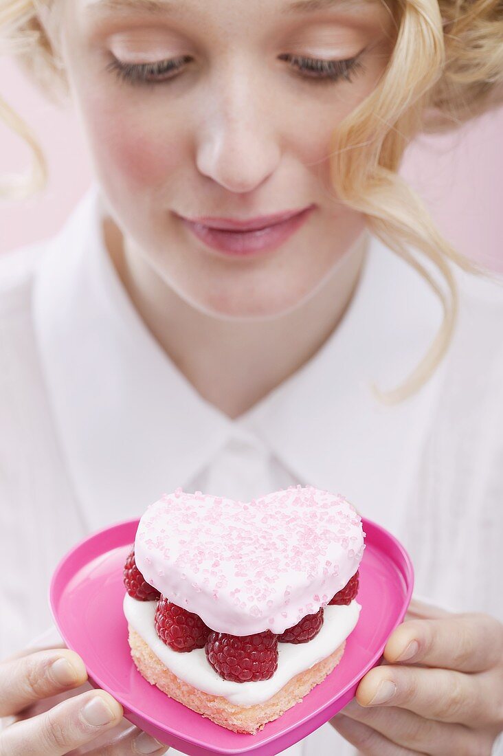 Young woman holding raspberry cake in heart-shaped dish