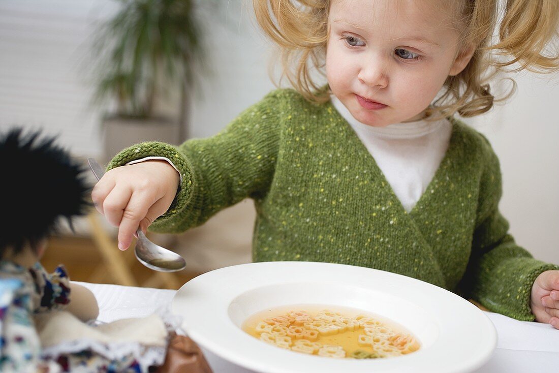 Small girl giving her doll a spoonful of soup