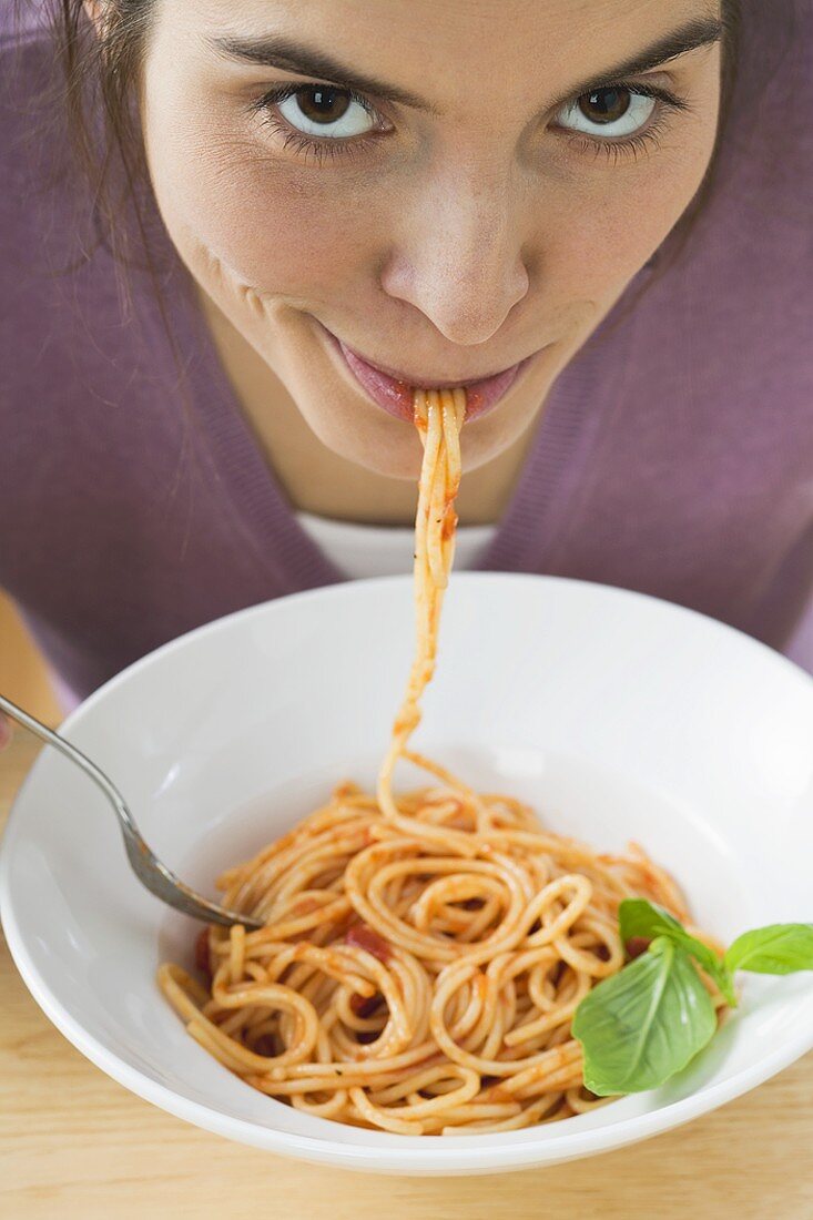 Young woman eating spaghetti with tomato sauce