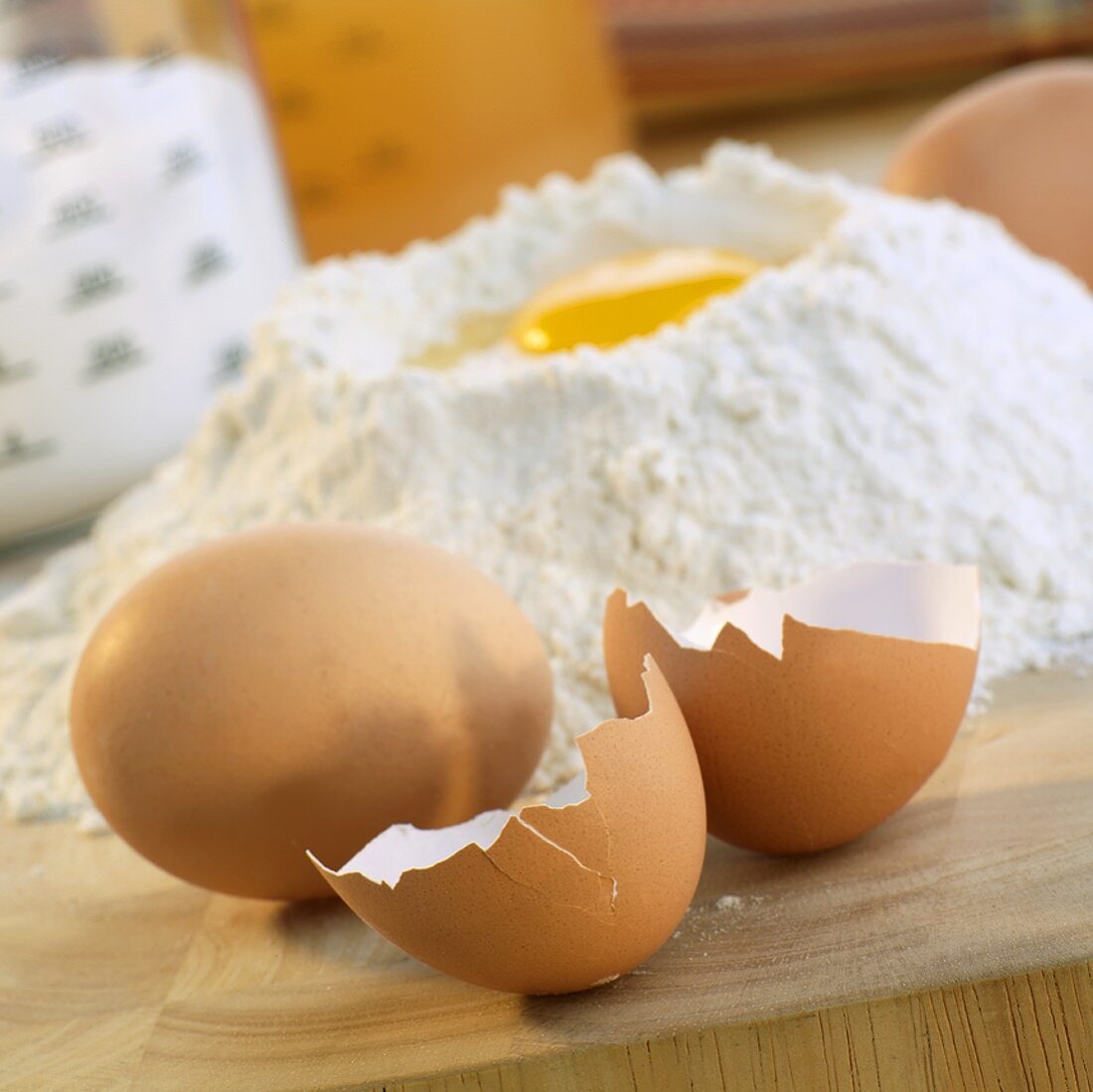Eierschalen und ganzes Ei, dahinter Mehlmulde mit Ei