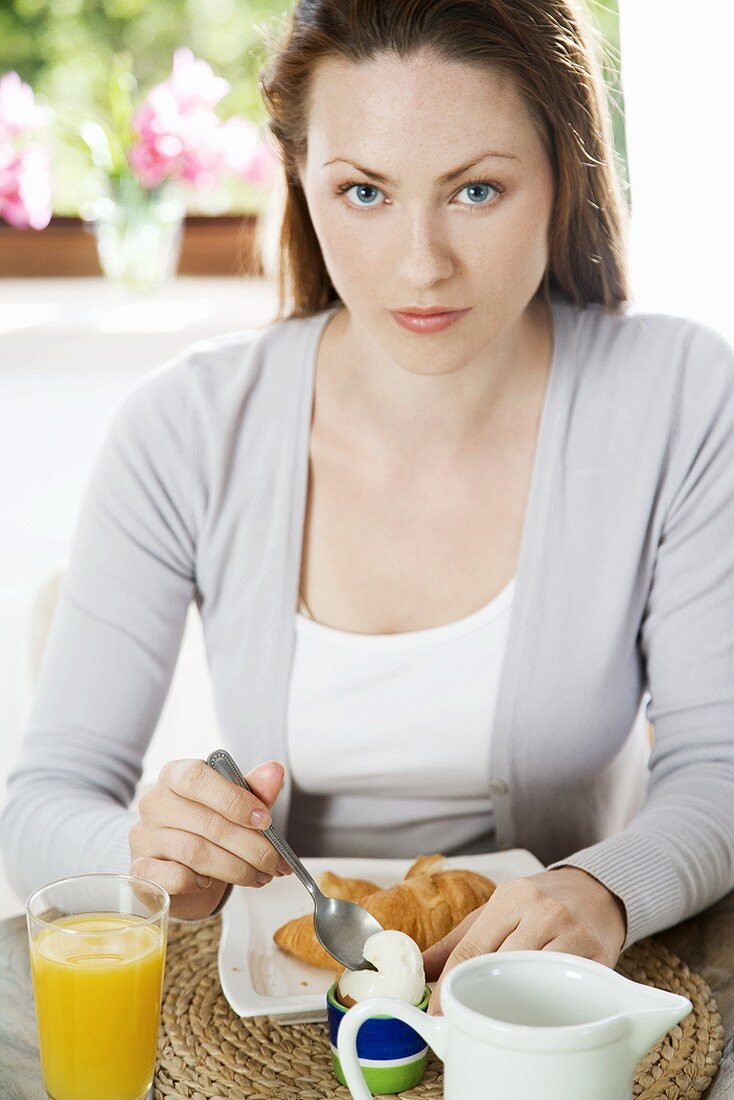 Young woman eating boiled egg for breakfast