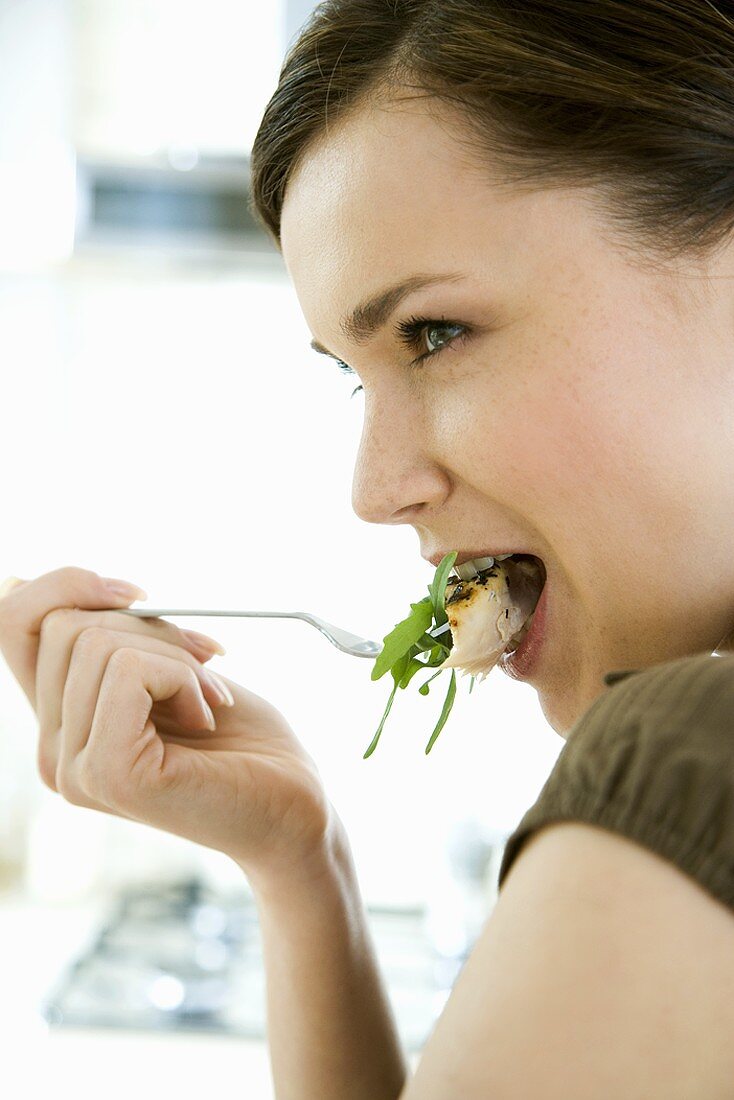 Young woman eating chicken breast with rocket