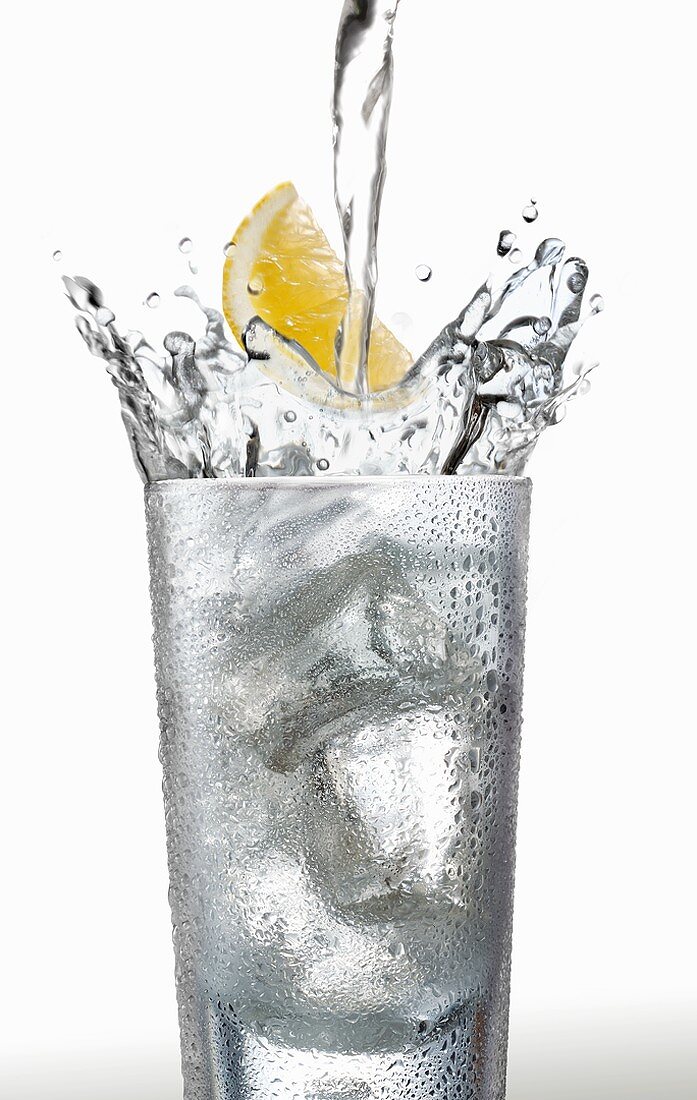 Wasser mit Zitronenschnitz in ein Glas gießen