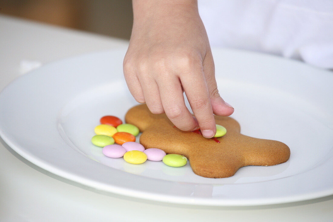 Kinderhand verziert Lebkuchenfigur mit Schokolinsen