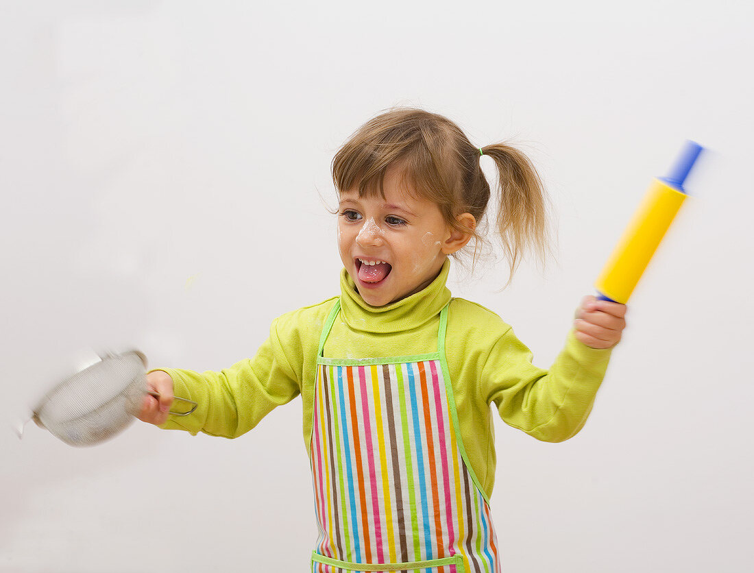 Girl in apron with rolling pin and sieve