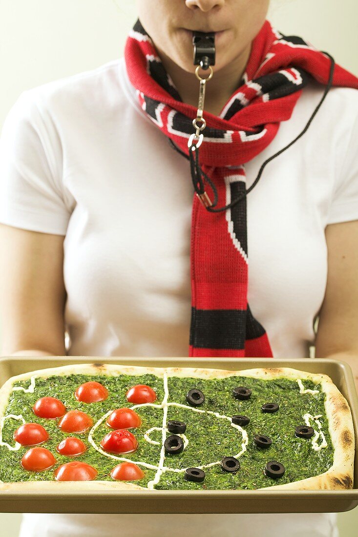 Spinatpizza mit Tomaten und Oliven als Fussballfeld