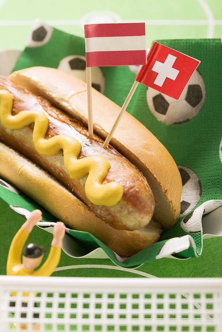 Bratwurst mit Senf in Brötchen, Flaggen und Fussballfigur