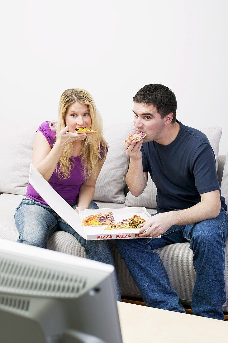 Junges Paar sitzt mit Pizza vor dem Fernseher