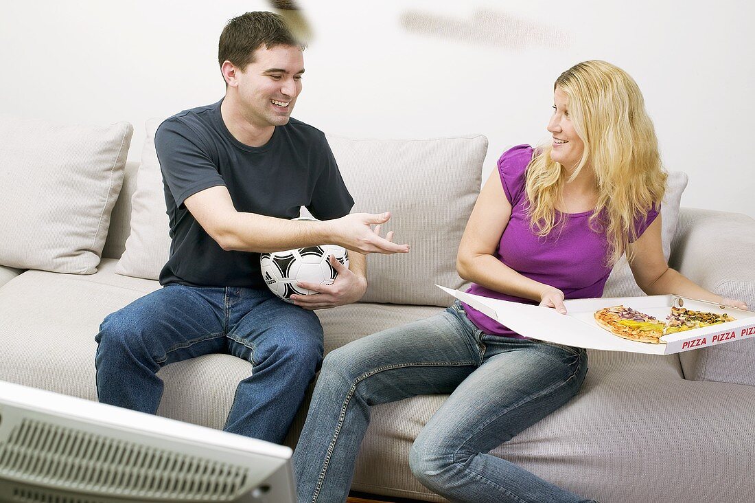 Young couple with pizza & football sitting in front of TV