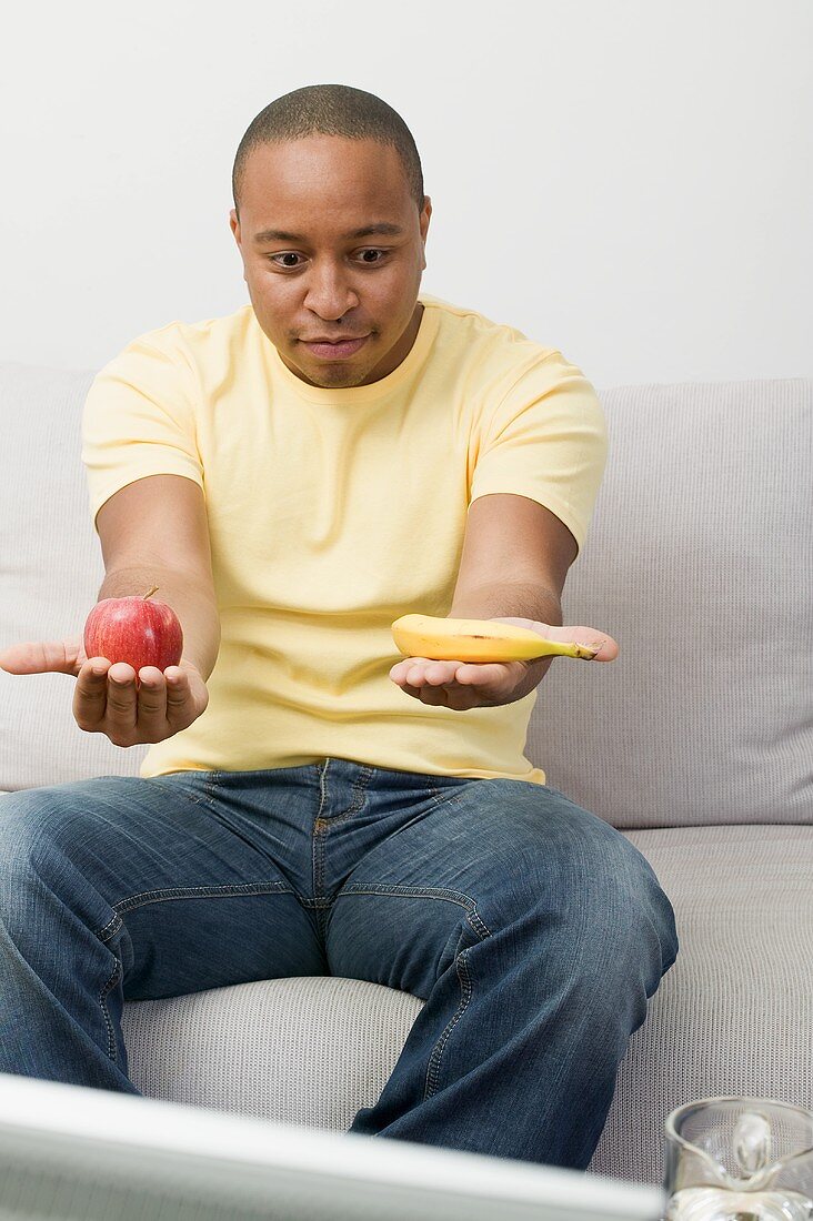 Young man with apple and banana watching TV