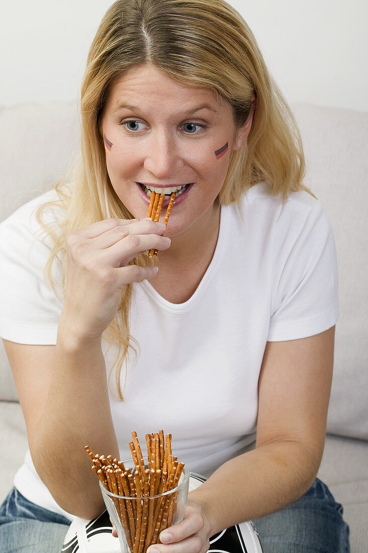 Young woman sitting on sofa with football & salted sticks