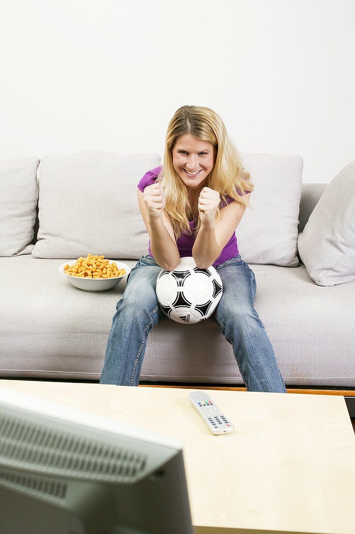 Junge Frau mit Fussball und Chips beim Fernsehen