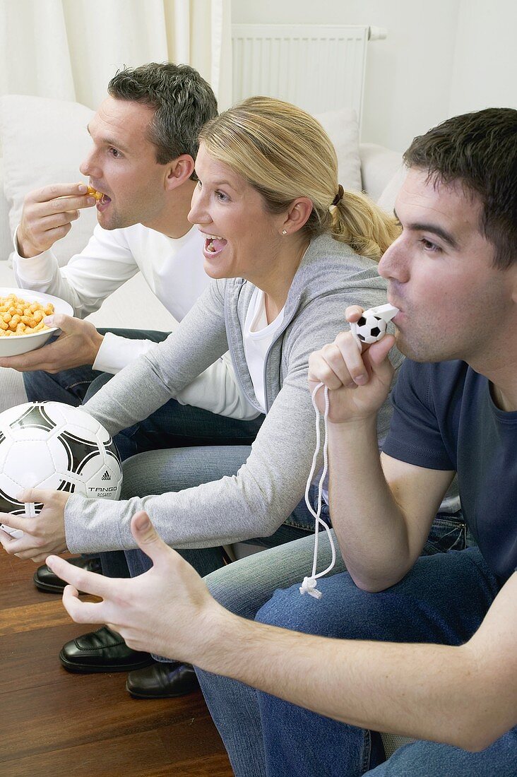 Friends watching TV with referee's whistle, football & crisps