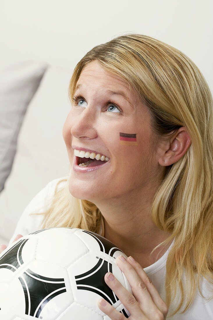 Junge Frau mit Deutschland-Farben im Gesicht hält Fussball