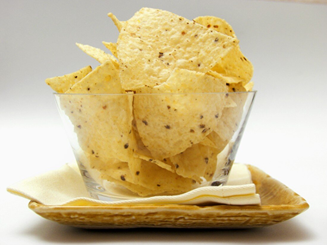 Tortilla Chips in a Glass Dish Resting on a Plate with Napkin