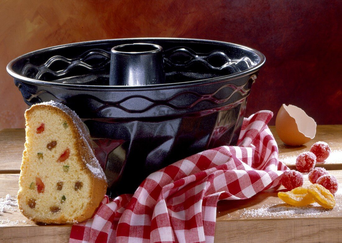 Piece of gugelhupf with candied fruit in front of baking tin