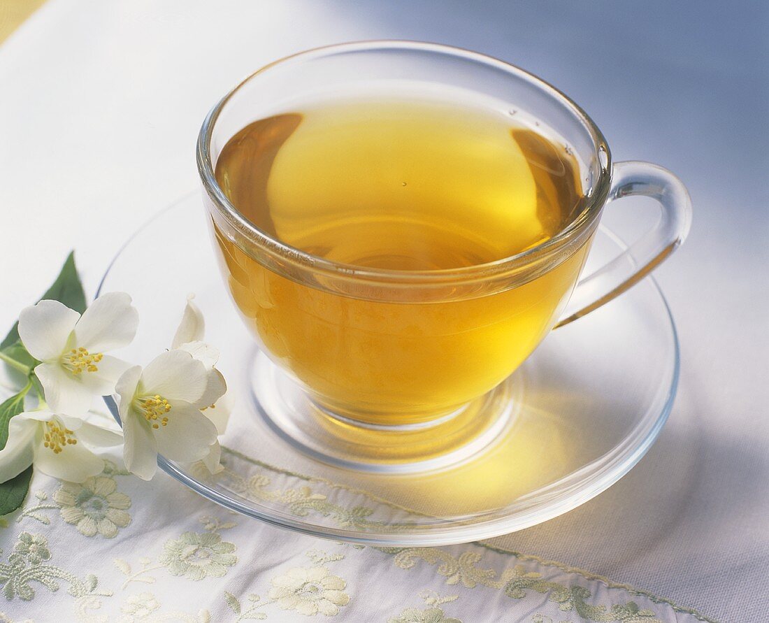 A cup of green tea, jasmine flowers beside it