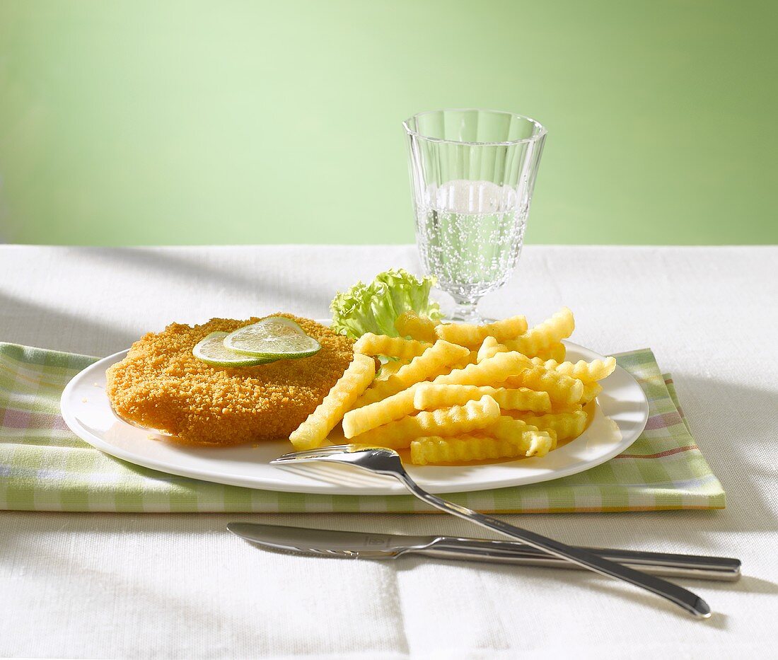 Escalope á la viennoise with lime slices, chips and a glass of water