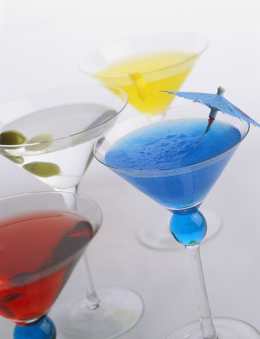 Vier verschiedene, bunte Cocktails in Martinigläsern
