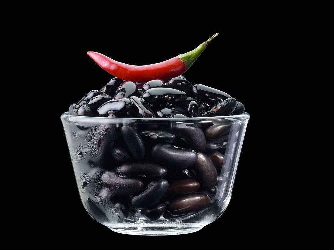 Schwarze Bohnen und rote Chilischote in Glasschale