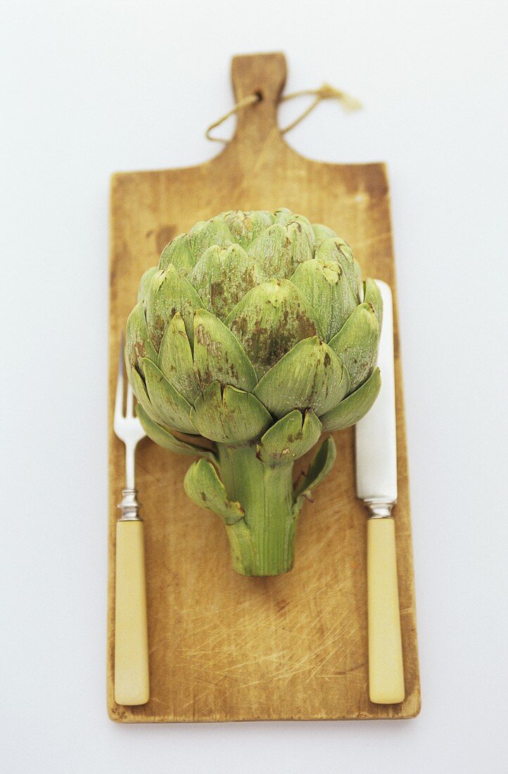 Artichoke with knife and fork on chopping board
