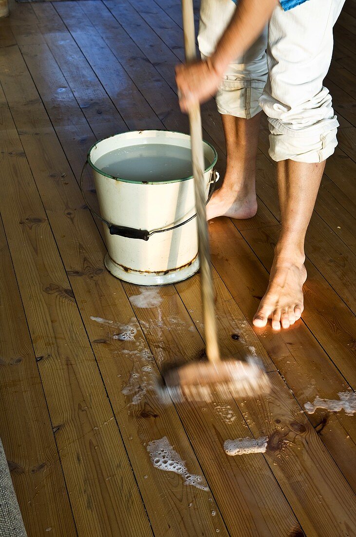Mann schrubbt den Holzboden mit Besen