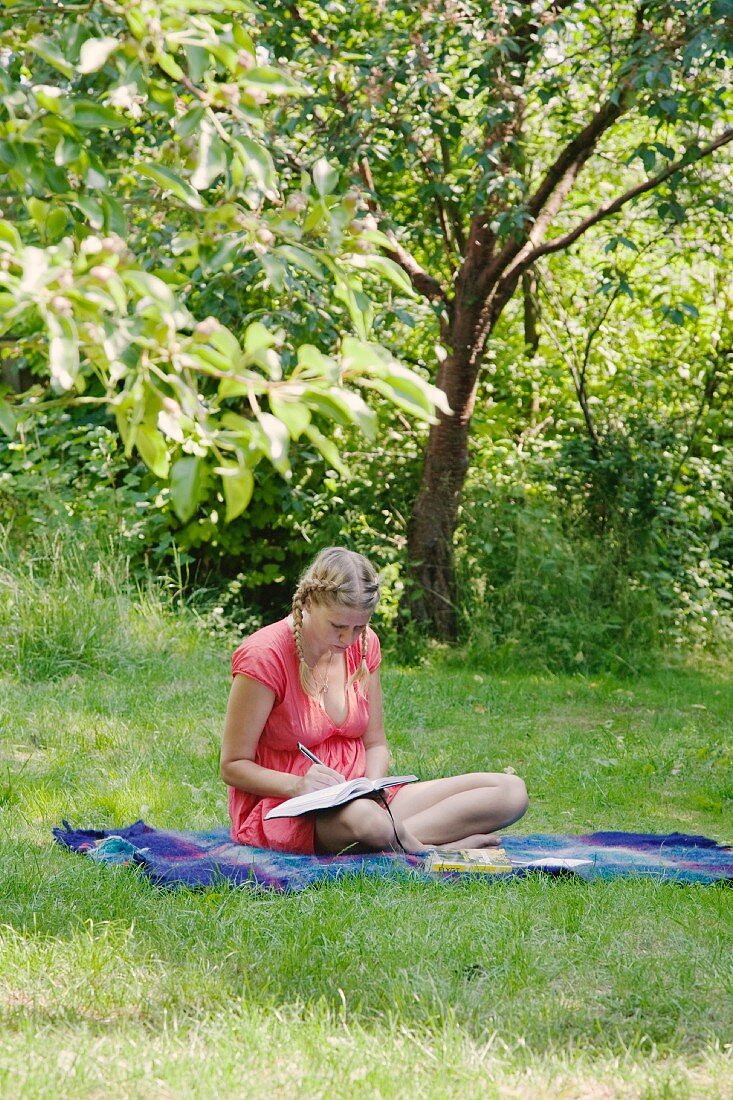 Schreibende Frau auf Decke im Gras