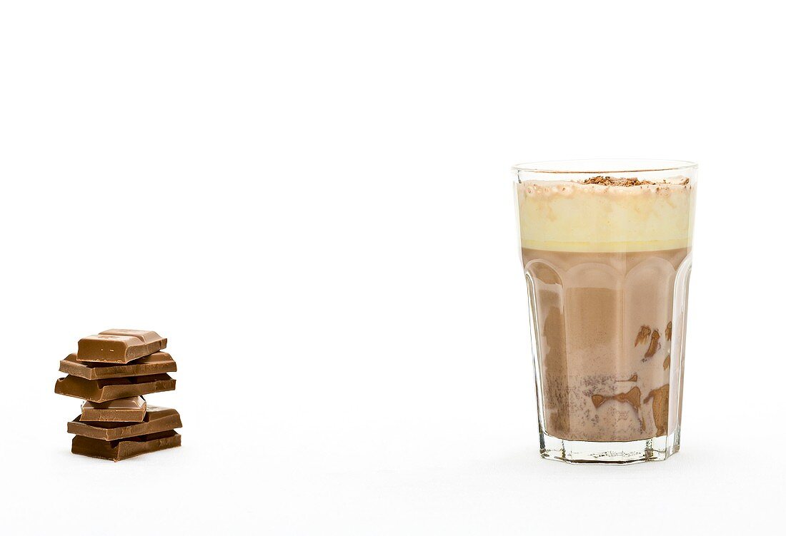 A glass of hot chocolate with pieces of chocolate next to it