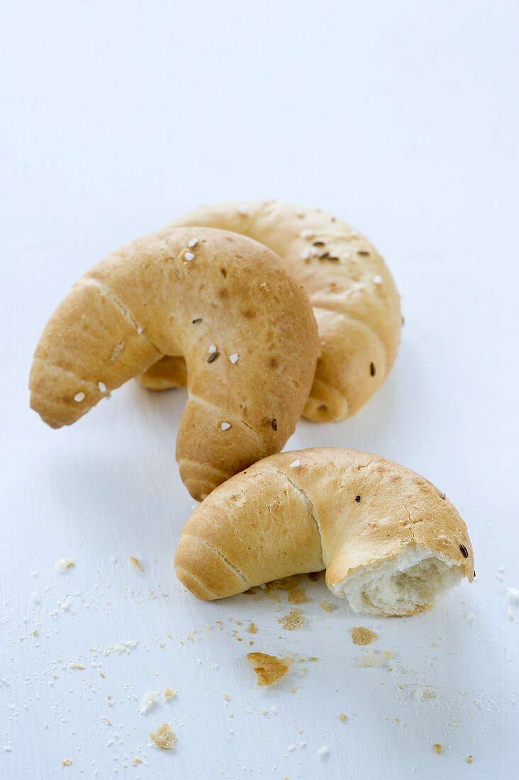 Three cresent shaped rolls with salt and caraway, whole and bitten