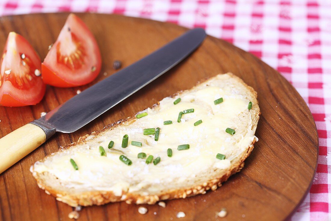 A slice of bread spread with butter and chives on wooden plate