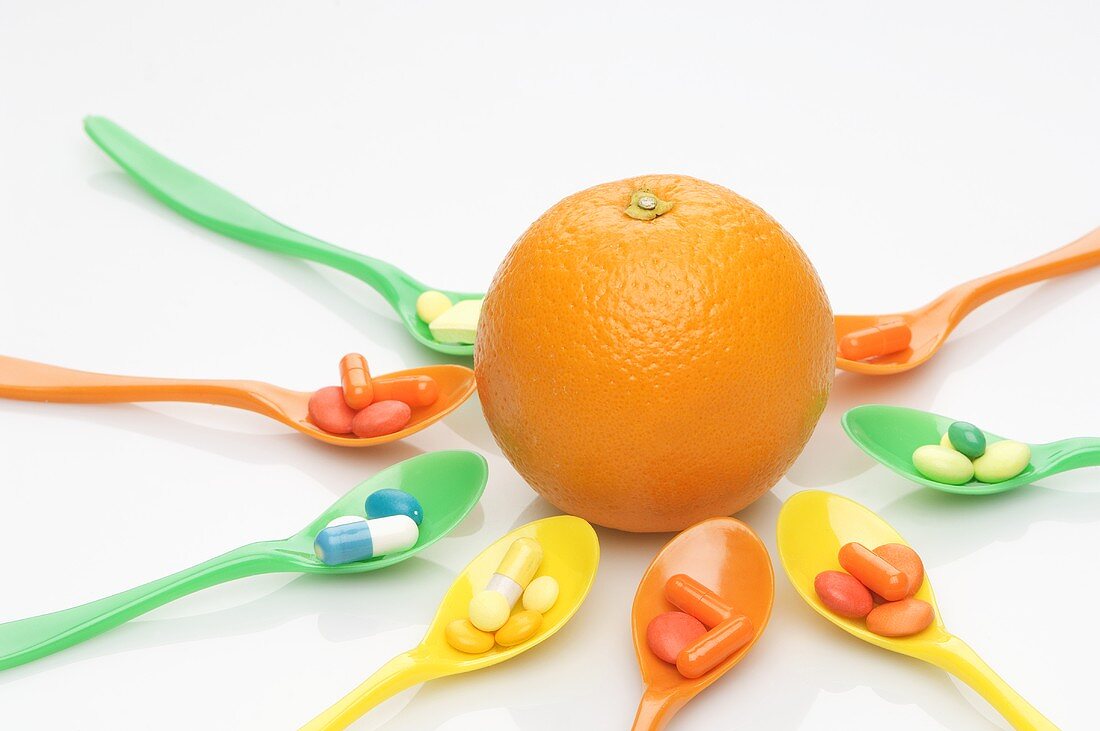Spoons with vitamin tablets around an orange