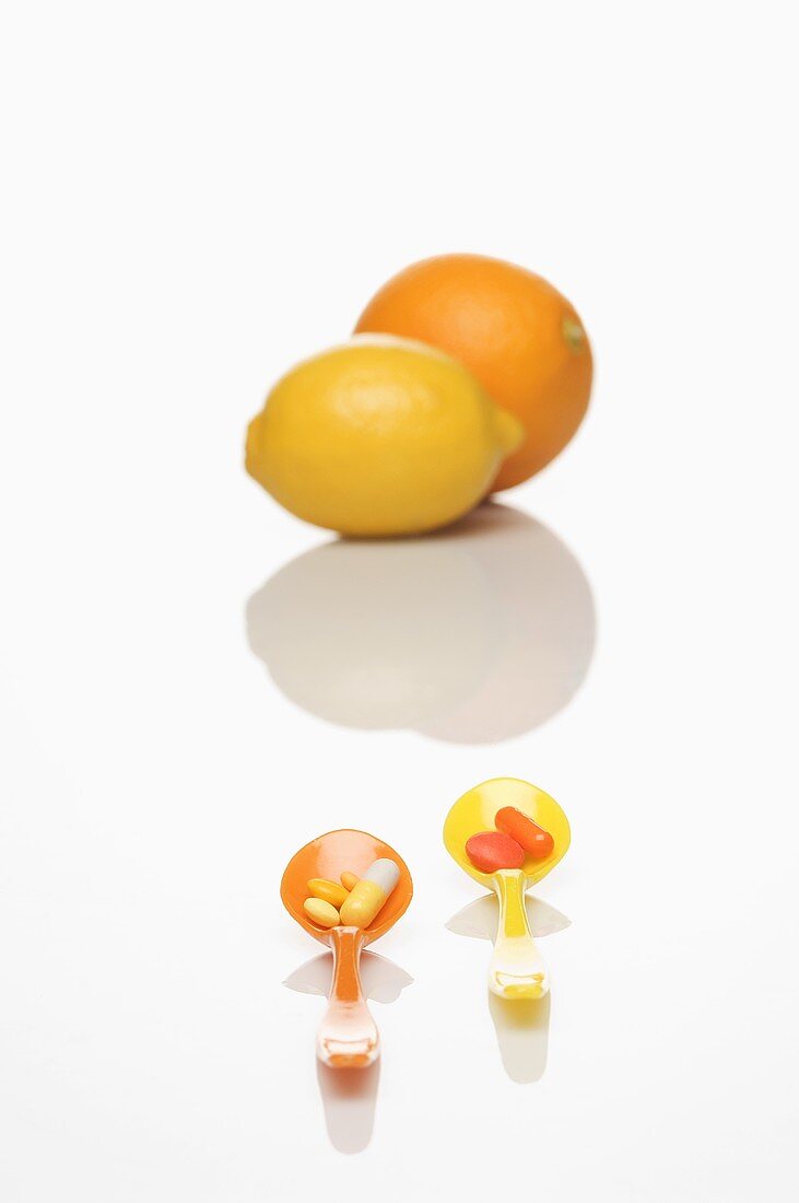 Spoons with vitamin tablets, a lemon and an orange