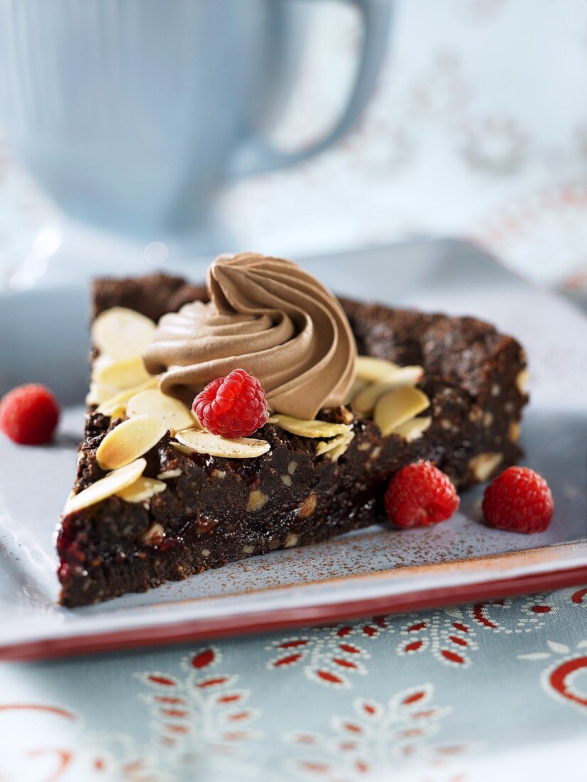 A slice of chocolate cake with slivered almonds and raspberries