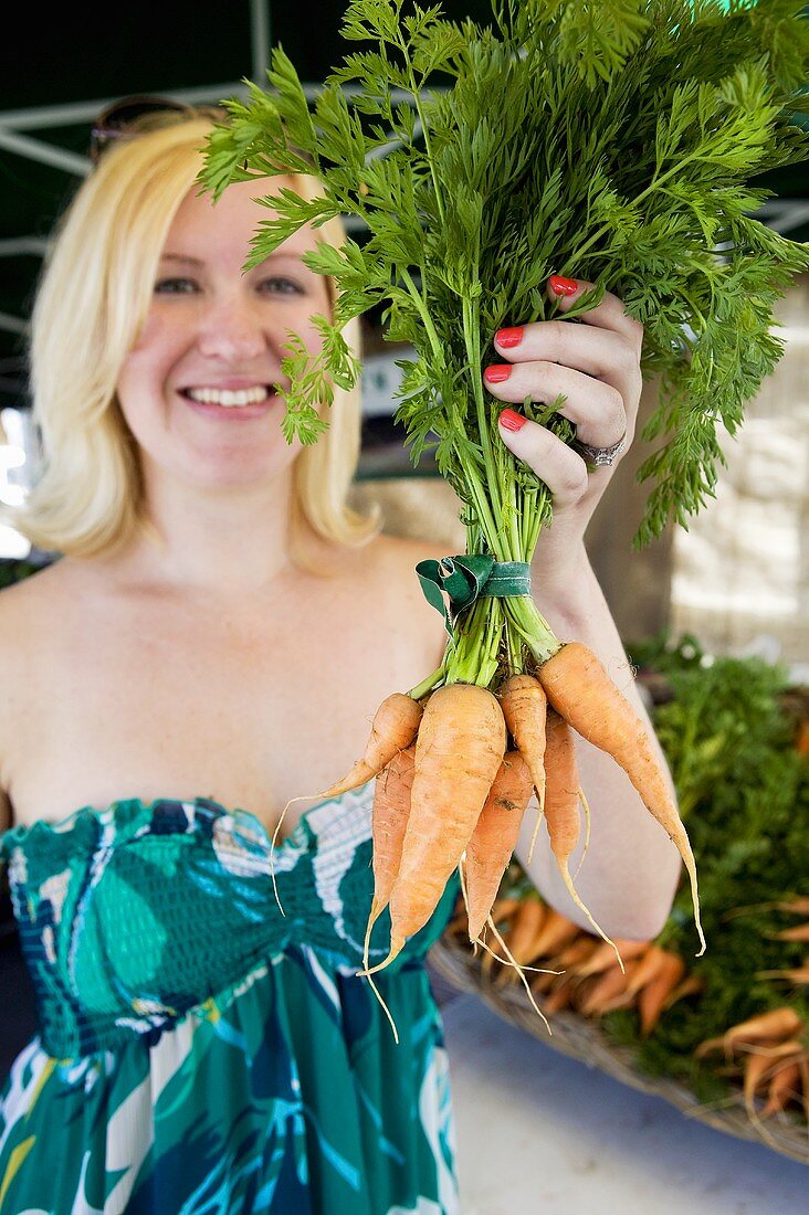 A woman holding a bunch of carrots at a market
