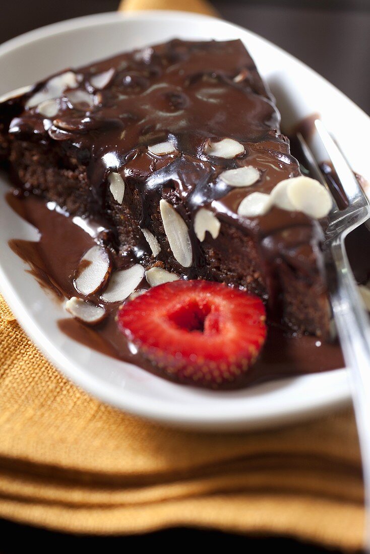 A piece of chocolate cake with chocolate sauce, slivered almonds and strawberries
