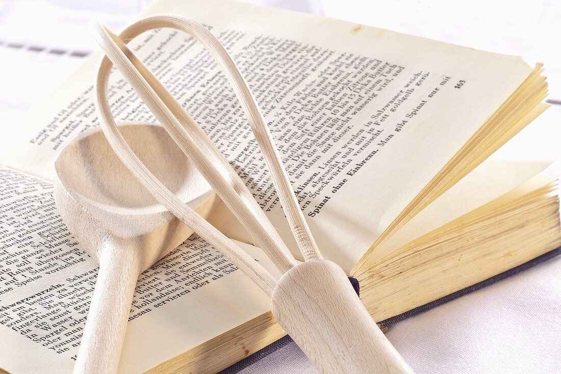 A cookbook, a whisk and a wooden spoon