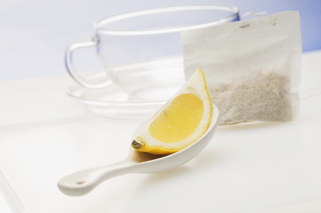 A lemon wedge on a spoon, a tea bag and a tea cup