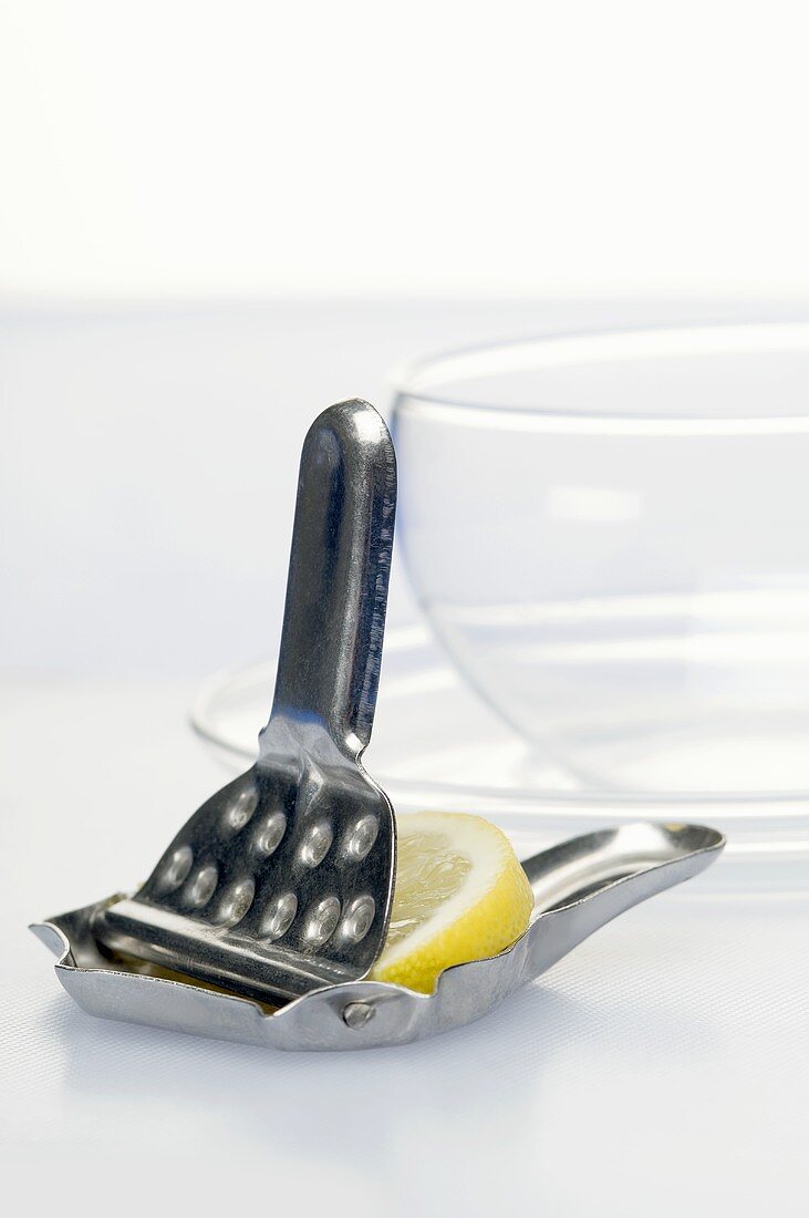 A lemon press with a slice of lemon and a tea glass in the background