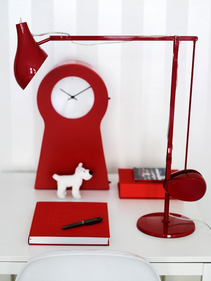 A white desk with a red lamp, clock, note book and a toy dog