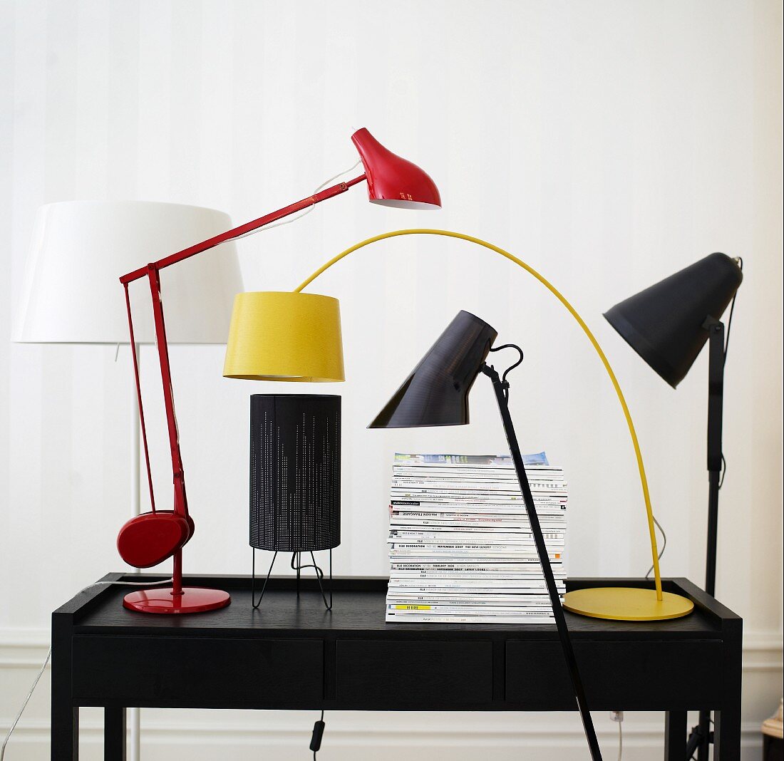 Various designer lamps and a stack of newspapers on a desk