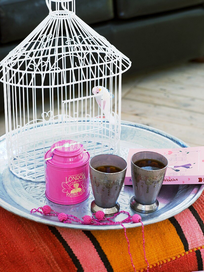 A bird cage and tea cups on a tray