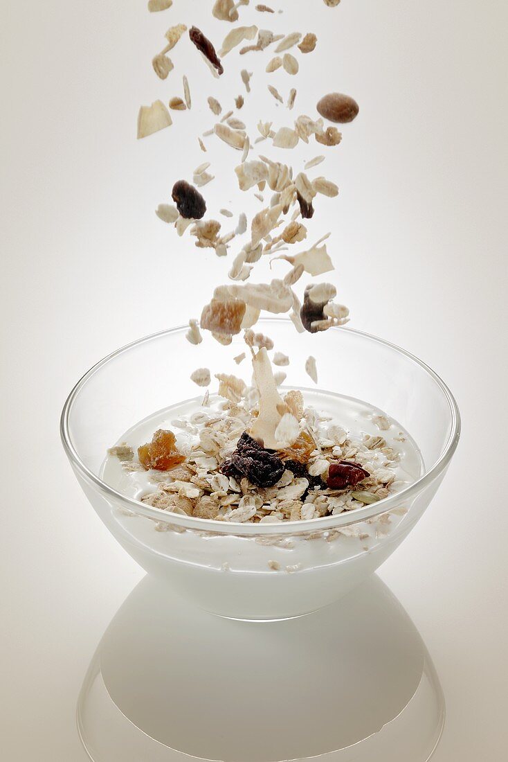 Muesli ingredients (cereals and dried fruit) falling into a bowl of yogurt