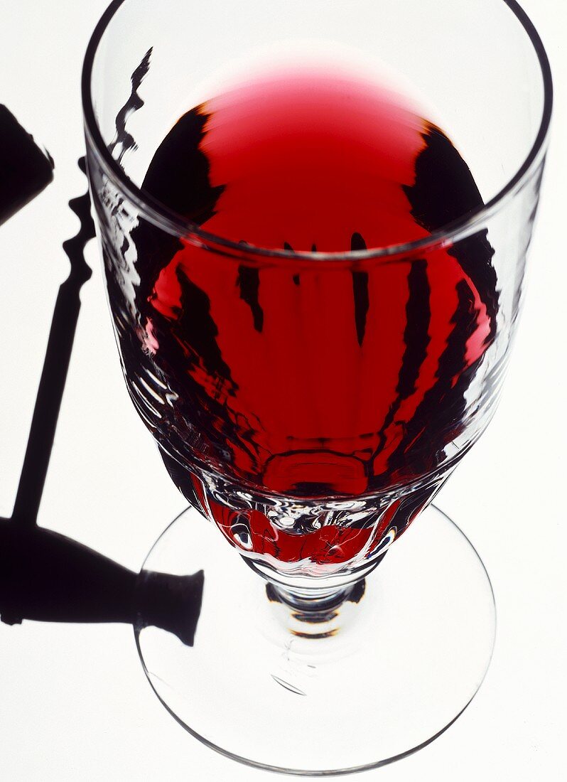 A glass of red wine and a corkscrew (transmitted light)