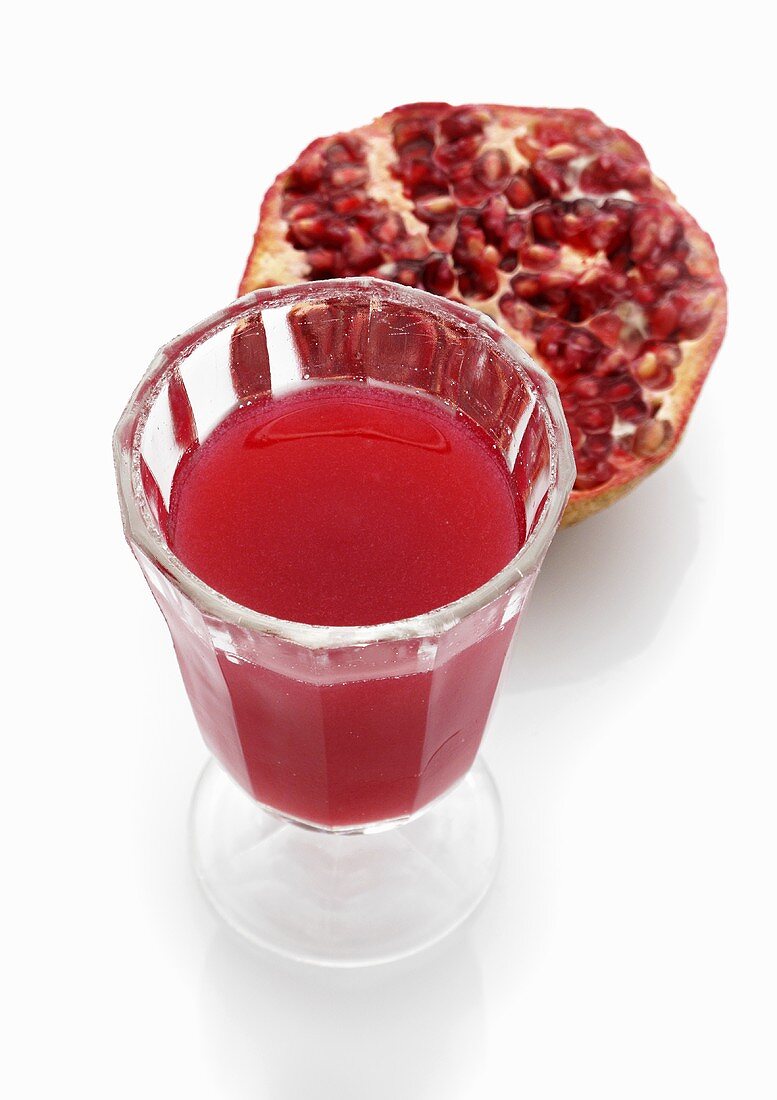 A glass of pomegranate juice with half a pomegranate in the background